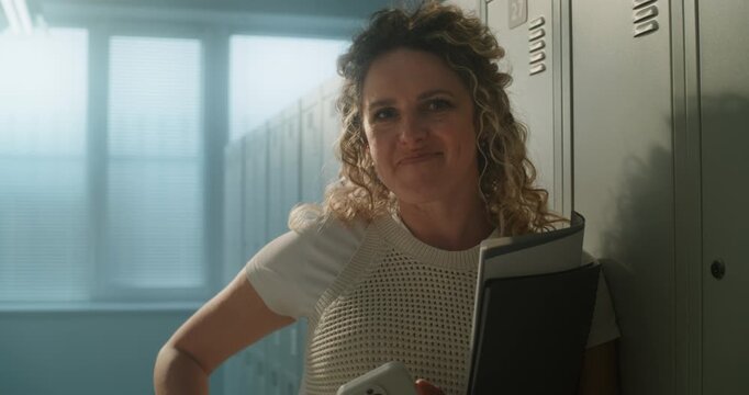 Portrait of Smiling Female Teacher Standing in Empty School Locker Room While Holding Notebooks and Smartphone. Concept of Teaching, Digital Communication, Work Life Balance, Modern School Life.