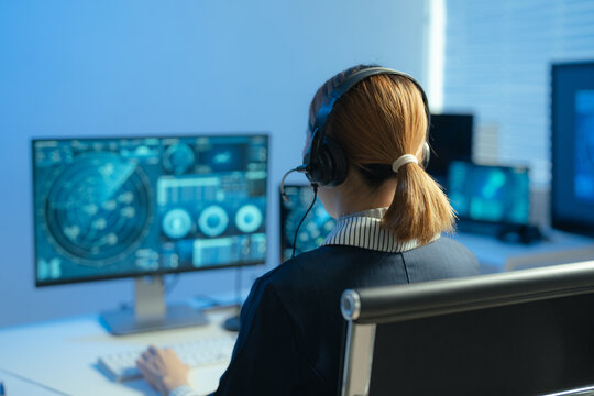 Female air traffic controller monitors flight radar screens in a modern dark command center, aviation technology, flight safety, surveillance and precision.
