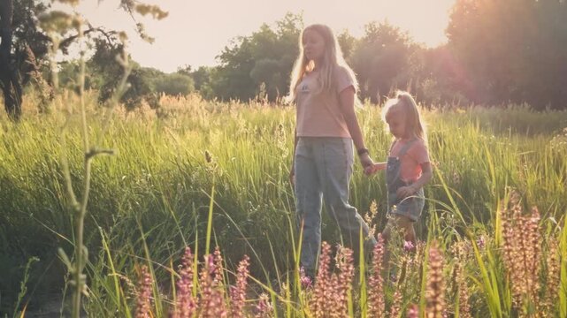 Mother and daughter enjoying a peaceful walk through a blooming summer wildflower field in sunny rural Ukraine. Tender family bonding, motherhood, scenic natural landscape.