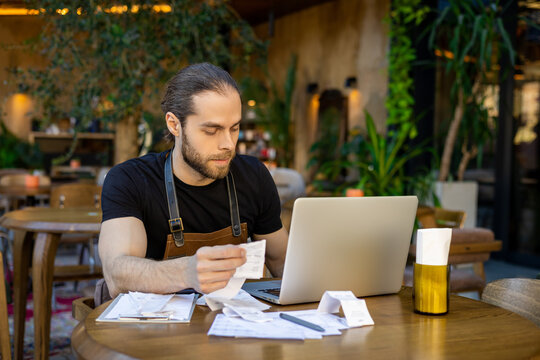 Focused male cafe owner checking bills