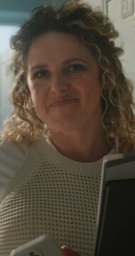 Portrait of Smiling Female Teacher Standing in Empty School Locker Room While Holding Notebooks and Smartphone. Teaching, Digital Communication, Work Life Balance, Modern School Life. Vertical Shot.