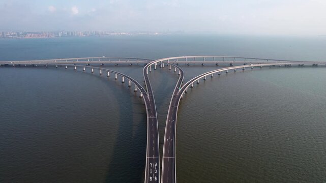 Aerial shot of a long curved bridge spanning across calm water, connecting land areas in the distance.