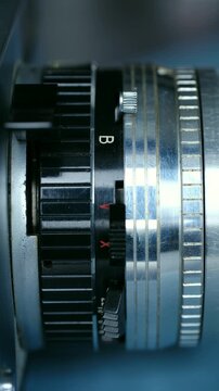 Close up view of a photographer hand adjusting the shutter speed dial on a classic manual film camera lens, selecting the bulb mode and other settings for creative photography. Vertical video