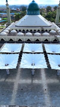Aerial view of Balikpapan Islamic Center with its prominent green dome and large white retractable umbrellas in the courtyard in Balikpapan, East Kalimantan, Indonesia.