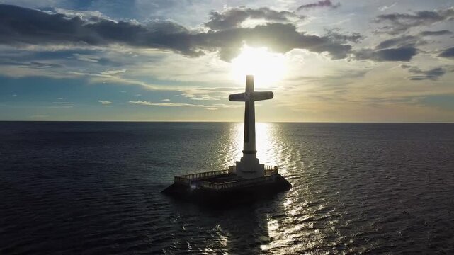 Aerial view of the Sunken Cemetery cross standing in the sea at sunset with golden light reflecting on the water in Catarman, Camiguin, Philippines.