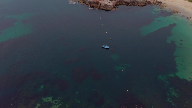 Aerial drone view of a small fishing boat moored in the clear turquoise bay of A Lanzada beach over a rocky seabed in Pontevedra Galicia Spain