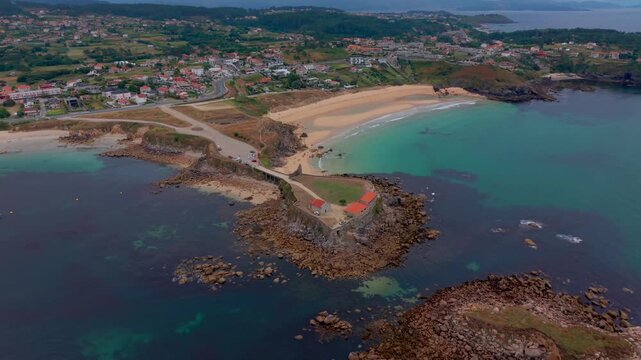Aerial drone view of the Nossa Senhora da Lanzada chapel headland with rocky outcrops turquoise water and the long A Lanzada beach in Galicia Spain