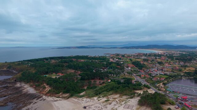 Aerial drone view of a wide beach with dunes green vegetation and a town overlooking Lanzada bay at Sanxenxo in Galicia Spain