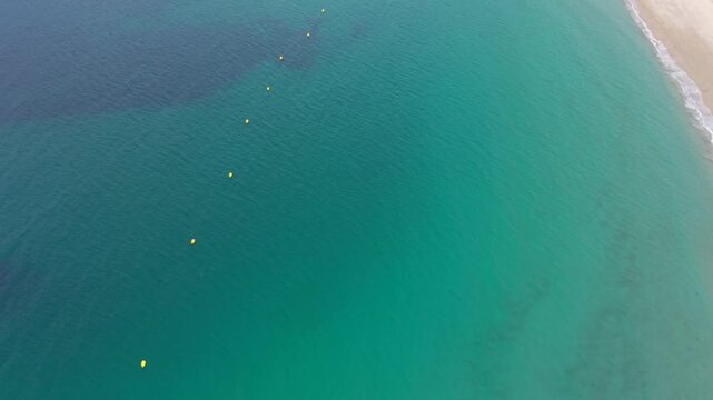 Aerial - turquoise shallows a line of yellow buoys and breaking surf off the beach at Sanxenxo