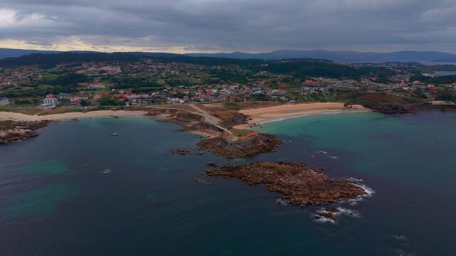 Aerial drone view of the rocky headland reefs and beach around the Nossa Senhora da Lanzada chapel with a coastal town in Pontevedra Galicia Spain