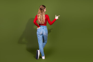 Naklejka premium Young woman in red top and jeans points with finger against green background