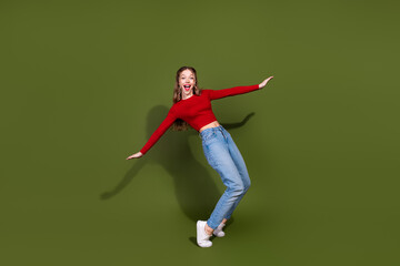 Naklejka premium Energetic young woman in red top and jeans leaps against a green background showing style and joy