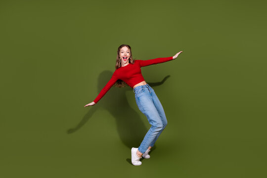 Energetic young woman in red top and jeans leaps against a green background showing style and joy