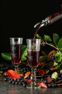 Black chokeberry drink is poured from a bottle into a glass.