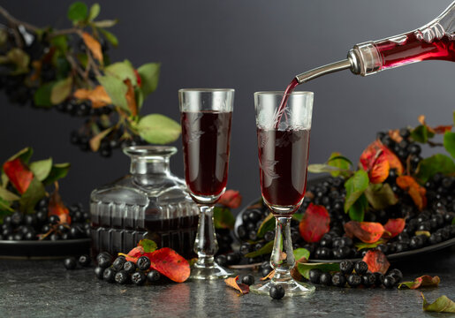 Black chokeberry liqueur and fresh berries on a black stone table.