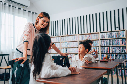 Happy school teacher and students having interesting engaging activities in class. Little children sitting around classroom table, talking and playing fun games together