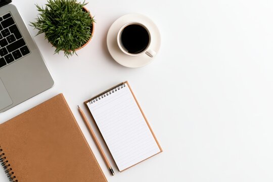 Top view of a clean white workspace with black coffee, notebook, pen, green plant, and generous copy space for text.