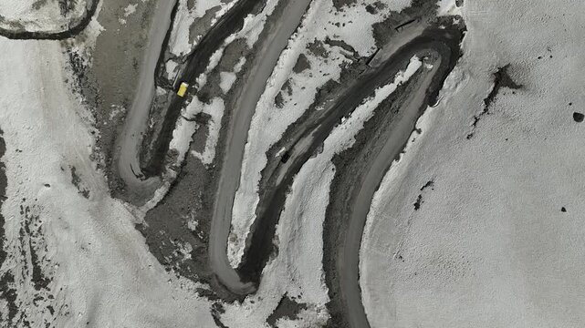 Aerial view of yellow truck driving through tight hairpin curves cut into snowfields at Shinku La Pass Zanskar shot by a drone
