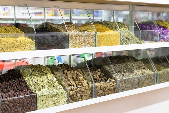 Spices and dried herbs displayed in glass compartments at a bazaar in Bukhara, Uzbekistan. Variety of colorful ground seasonings, roots, and dried flowers arranged on shelves for sale.