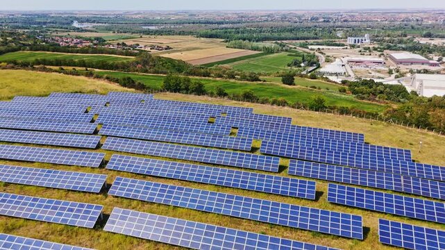 Aerial view of solar panel farm with rows of photovoltaic panels set in a rural landscape with green fields and industrial buildings Beocin, Vojvodina, Serbia.