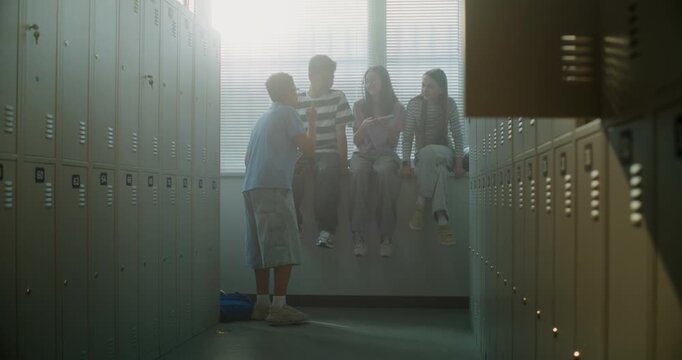 Teenage Boys and Girls Spend Time Together in School Locker Room, Sitting on Windowsill While Checking Smartphones, Socializing in Relaxed Atmosphere. Authentic Youth Lifestyle, Digital Communication.