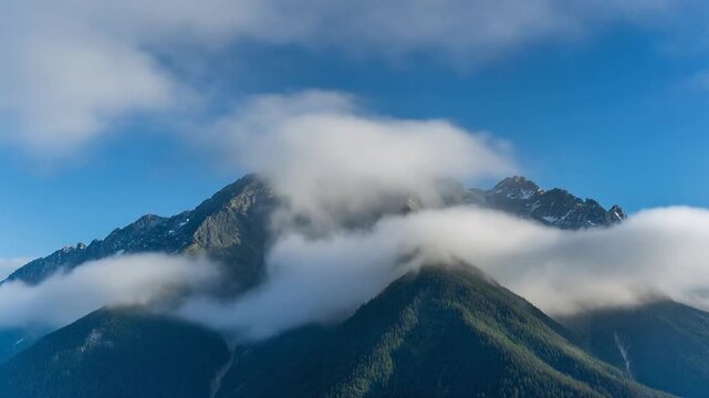 Wispy atmospheric clouds gracefully embrace the jagged peaks of a verdant mountain range under a vibrant azure sky, creating a breathtaking natural spectacle