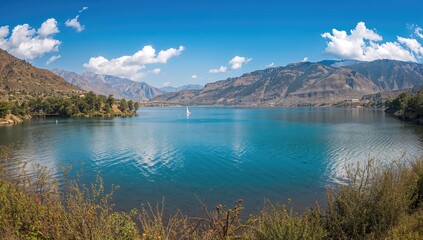 Naklejka premium Panoramic View of Serene Lake Surrounded by Mountains Under Blue Sky
