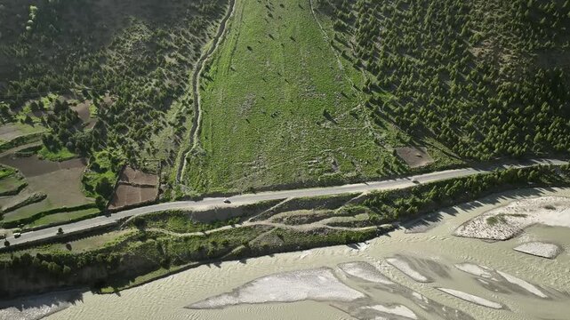 Aerial drone follow shot of cars on a riverside road through the Indian Himalayas near Jispa, Lahaul Valley, capturing remote mountain scenery, rugged terrain, flowing river 