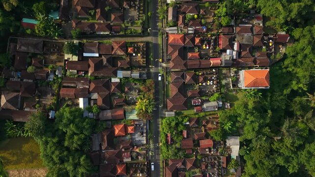 Aerial view of traditional Balinese village with red-tiled roofs, lush tropical greenery, and decorative penjor along the central road in Kecamatan Tegallalang, Bali, Indonesia.