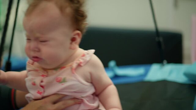 Little baby with a pink onesie expressing sadness and screaming during infancy. A parent's hand is holding her
