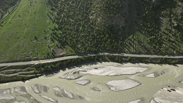 Drone follow video of car on a riverside road past a rural Himalayan village and farm terraces in Lahaul Valley India. Aerial view shot by a drone in himalayas
