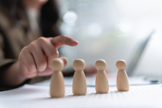 Businesswoman selecting wooden figures during hiring process, representing recruitment, candidate screening, talent selection, employee evaluation, human resources, workforce planning, and employment.