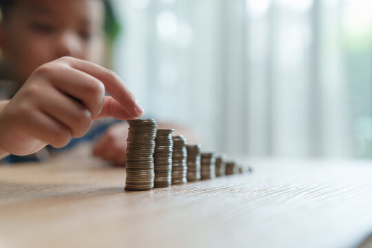 Asian Child stacking coins in ascending rows, representing saving, investment growth, financial planning, wealth building, future security, money management, financial goals.