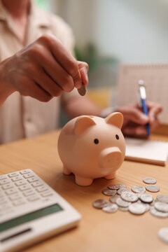 Man placing a coin into a piggy bank while planning finances with a calculator and notebook, representing saving money, budgeting, financial goals, emergency funds, retirement, and future planning.