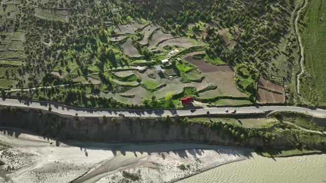 Aerial view by drone following a car on riverside road along with traditional stepped farm terraces and houses in a Himalayan valley near Jispa Lahaul Valley shot by a drone.