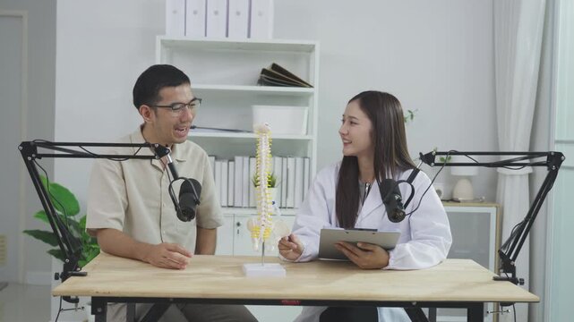 Female doctor explaining spine anatomy using a model to a male host during a medical podcast interview. Recording a healthcare broadcast in a studio. Orthopedics and chiropractic education concept.