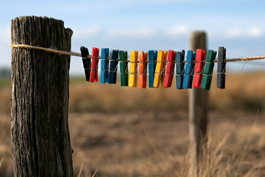 Vibrant colorful clothespins on a rope between rustic wooden posts against a blurry natural background.