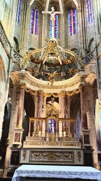 The elaborate golden altar is a striking feature within the Gothic architecture of the Basilique Saint Sauveur, located in Dinan, France. It is beautifully enhanced by colorful stained glass windows a