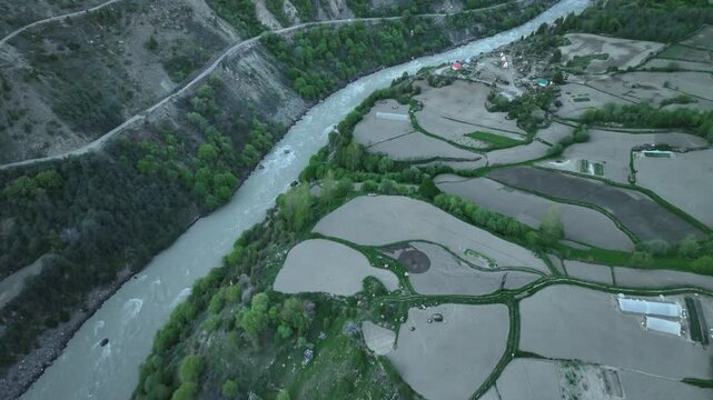 Aerial view of deep river gorge with a suspension bridge and a riverside campsite in India near Jispa Lahaul Valley shot by a drone
