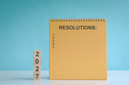 2027 on stacked wood blocks with list of resolutions. New year concept.