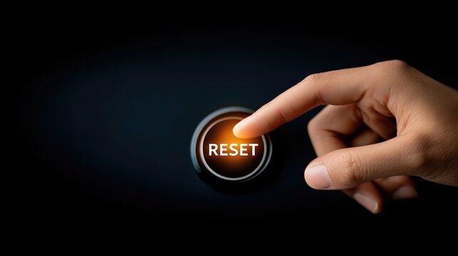 A finger presses a glowing reset button on a sleek control panel. Dramatic lighting and a dark background evoke restart, recovery, and fresh beginnings.