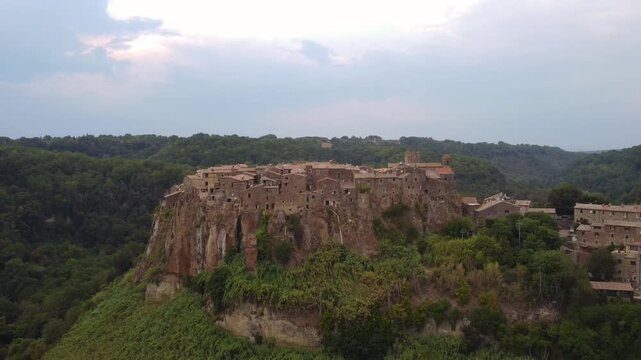 Aerial view of the historic hilltop village of Calcata Vecchia, featuring ancient stone buildings perched on a dramatic volcanic cliff surrounded by lush greenery in Calcata Vecchia, Lazio, Italy.