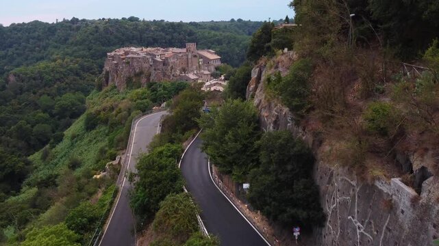 Aerial view of the historic hilltop village of Calcata Vecchia surrounded by lush green forests and winding roads in Calcata Vecchia, Lazio, Italy.
