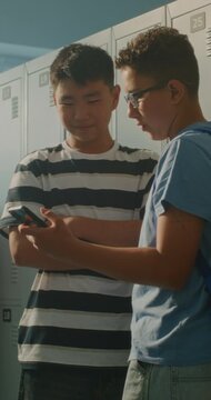 Friends Gathers around Smartphone near Lockers, Laughing Reacting Together as Two Girls Join Boys to Watch Entertaining Content. Friendship, Social Connection, Digital Communication. Vertical Shot.