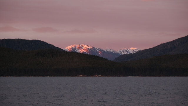 Breathtaking mountain glacier range view with luxury cruiseship cruise ship liner sailing in front of Alaska mountains Inside Passage transit with spectacular landscape scenery during sunset