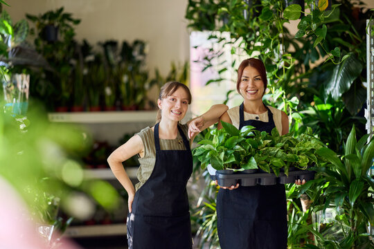 Two Smiling Plant Shop Employees Holding Potted Houseplants in a Bright Urban Nursery