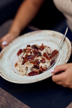 Creamy Pasta With Prosciutto Served In Rustic Bowl With Hands Holding Spoon At Outdoor Restaurant