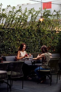 Two Friends Laughing and Dining Outdoors at a Cozy Rooftop Cafe Patio