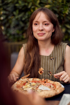 Young Woman Eating Pizza at Outdoor Cafe Smiling and Relaxed During Casual Lunch With Friends