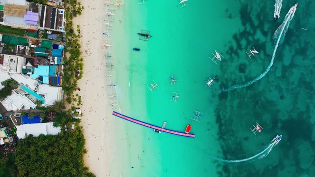 Top down drone slides left above the turquoise waters of White Beach, Boracay